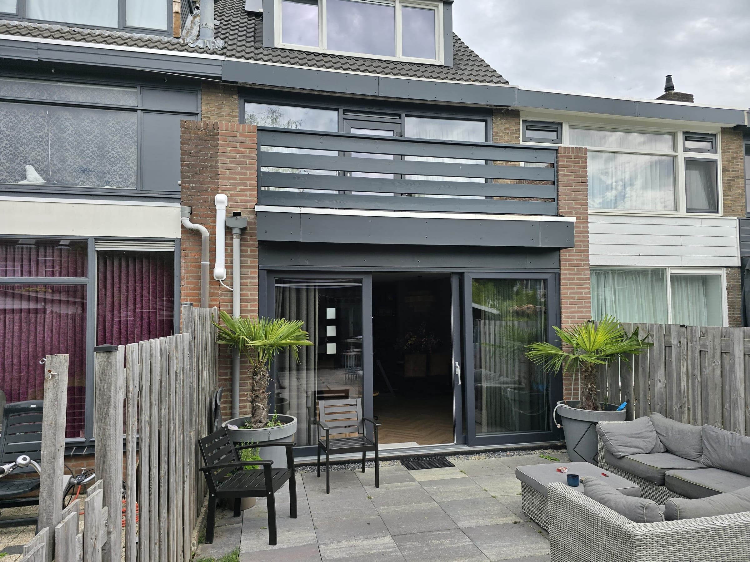 Gerealiseerde aanbouw aan de achterzijde van een rijtjeswoning, met brede schuifpui en antracietkleurige afwerking, door Flexora Bouw