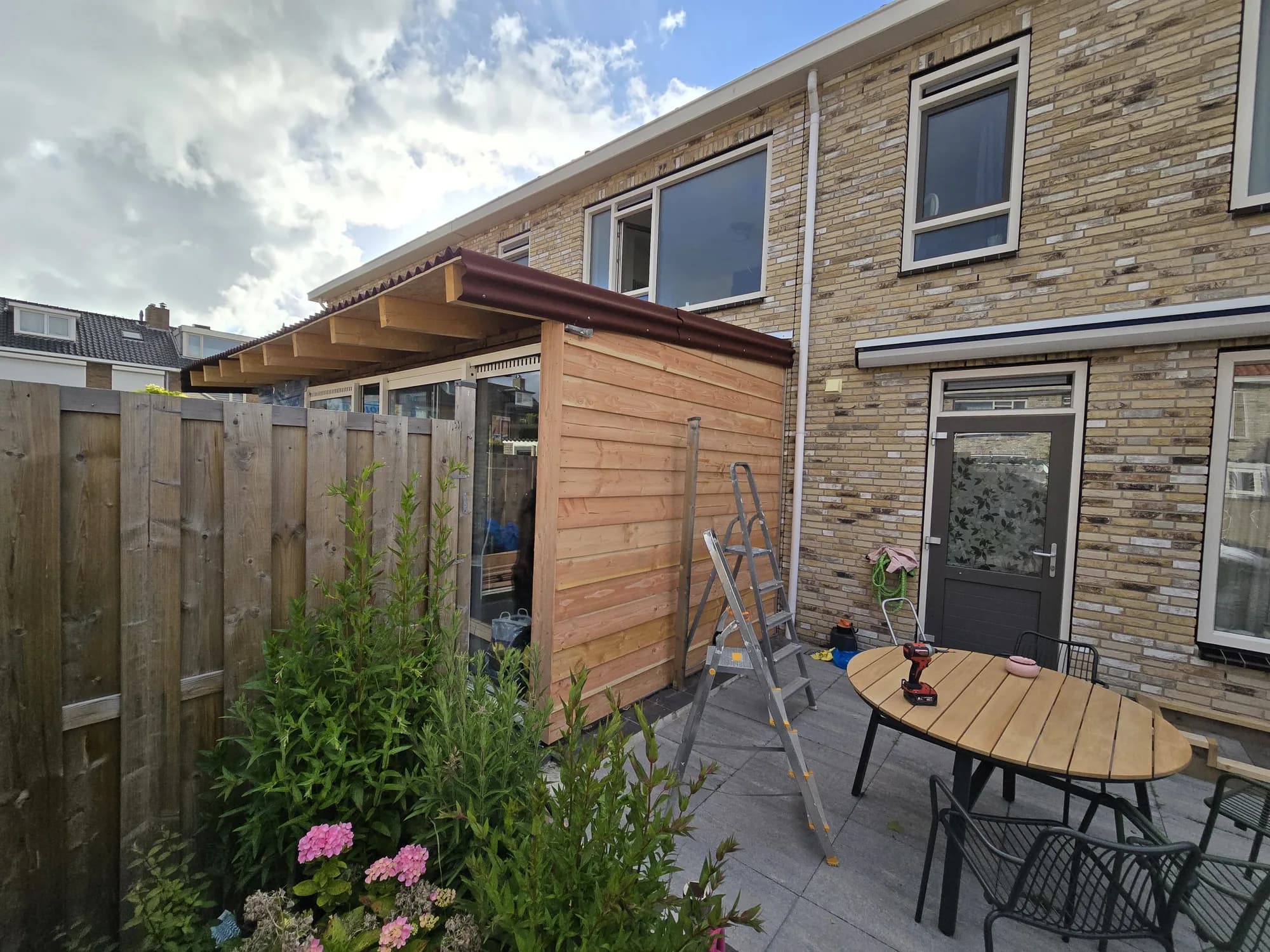 Houten aanbouw aan de achterzijde van een tussenwoning met terras en beplanting in de tuin