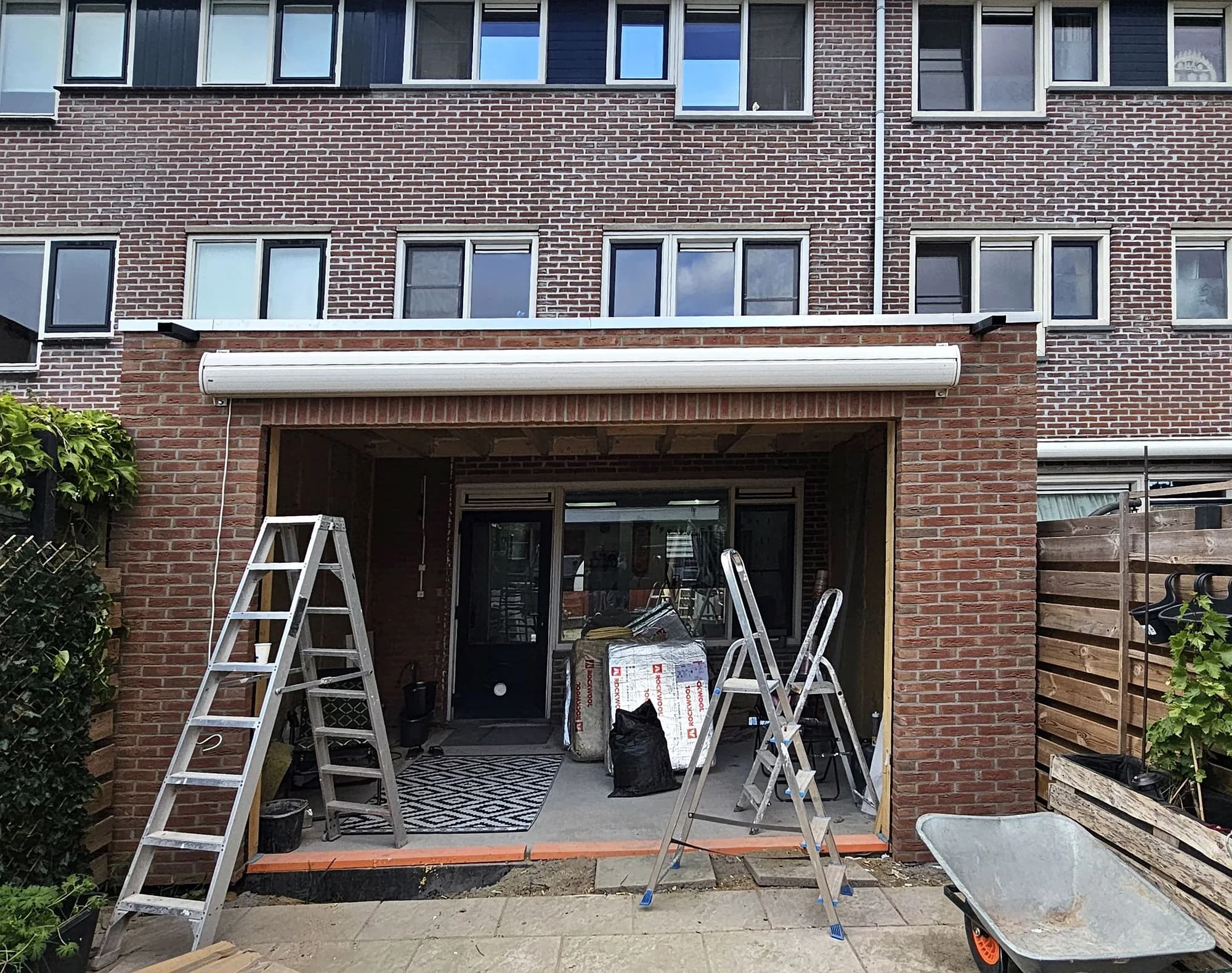 Gevelopening voor een nieuwe aanbouw met ladders en bouwmaterialen aan de achterzijde van een woning