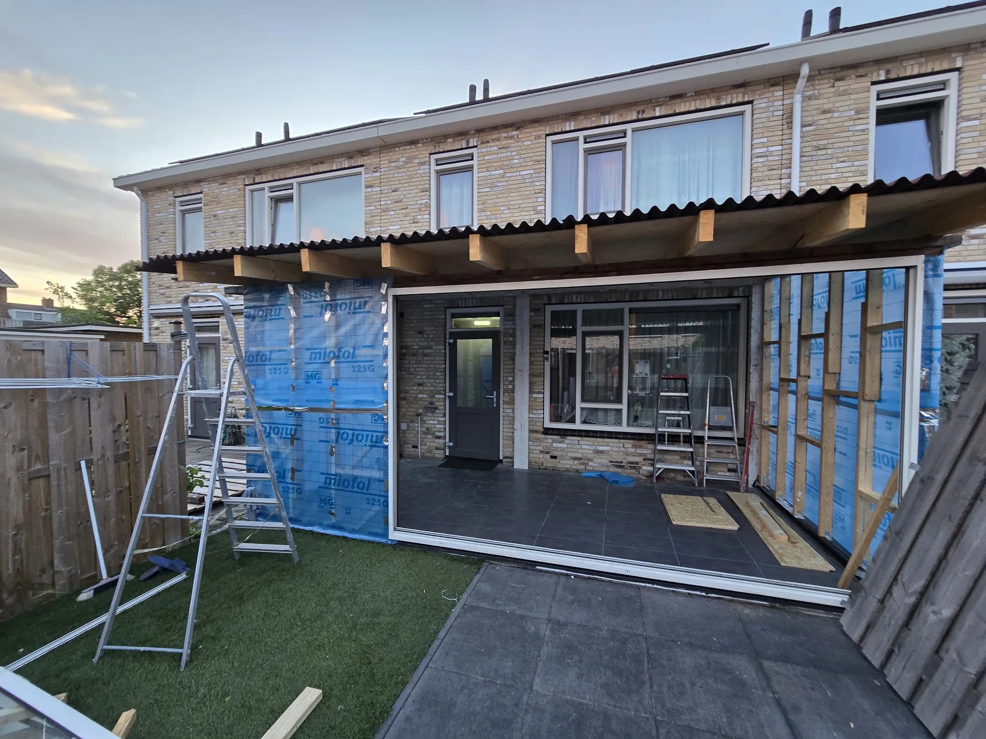Aanbouw in aanbouw met houten dakconstructie, dampfolie en ladders aan de achtergevel