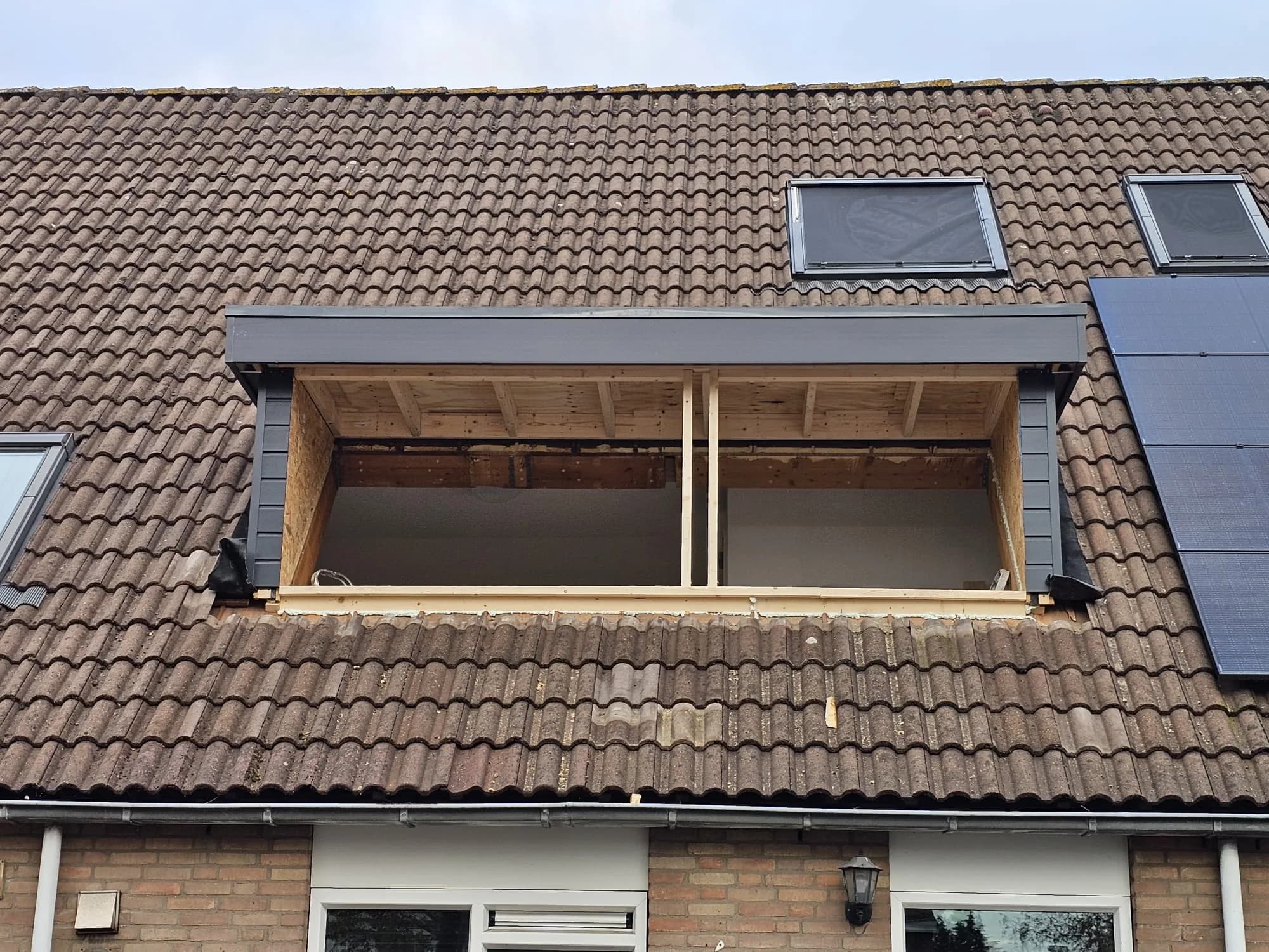 Dakopening in een pannendak tijdens werkzaamheden aan de nieuwe dakconstructie, met zonnepanelen ernaast