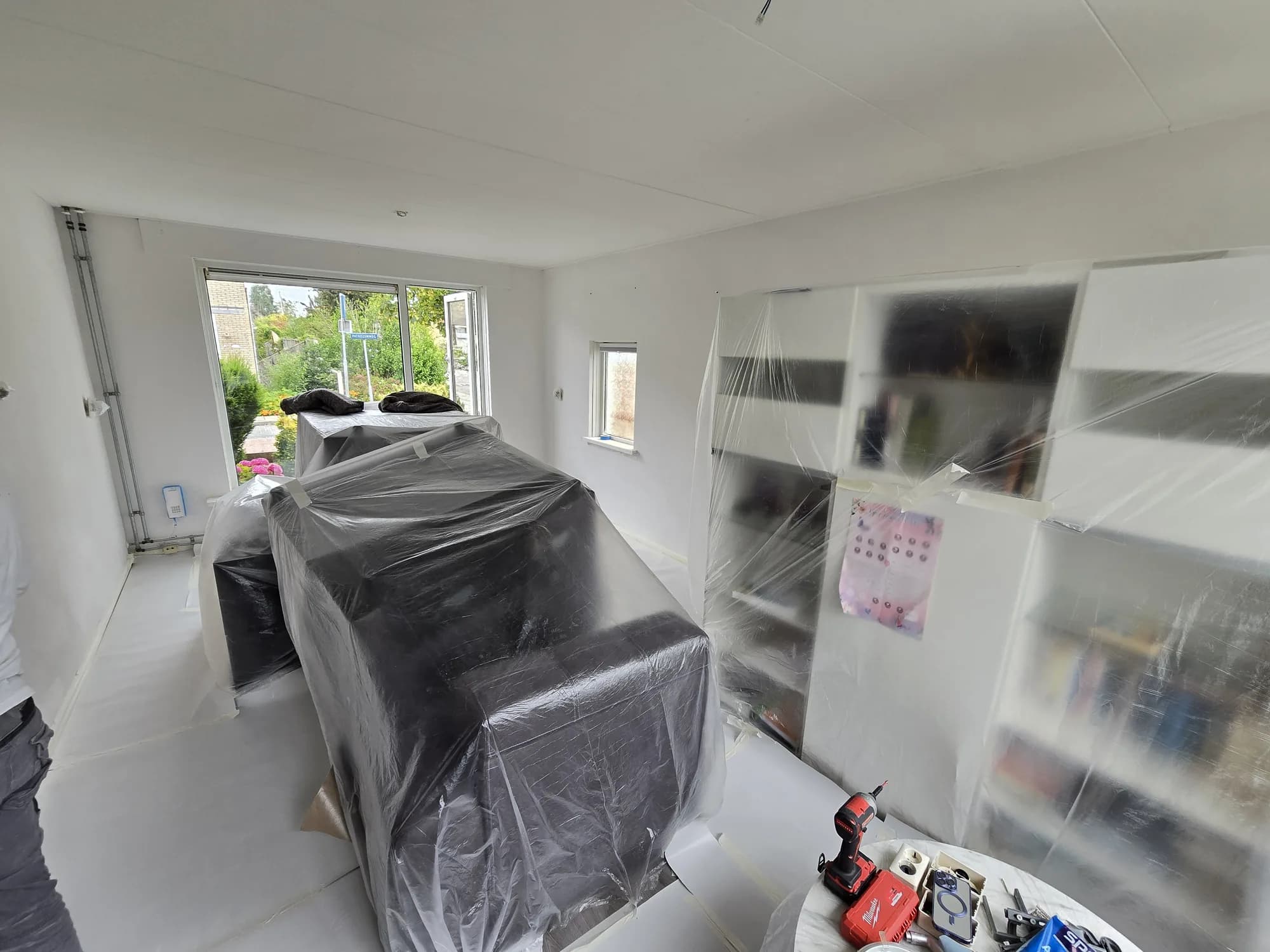 Woonkamer tijdens een verbouwing met meubels afgedekt onder plastic folie