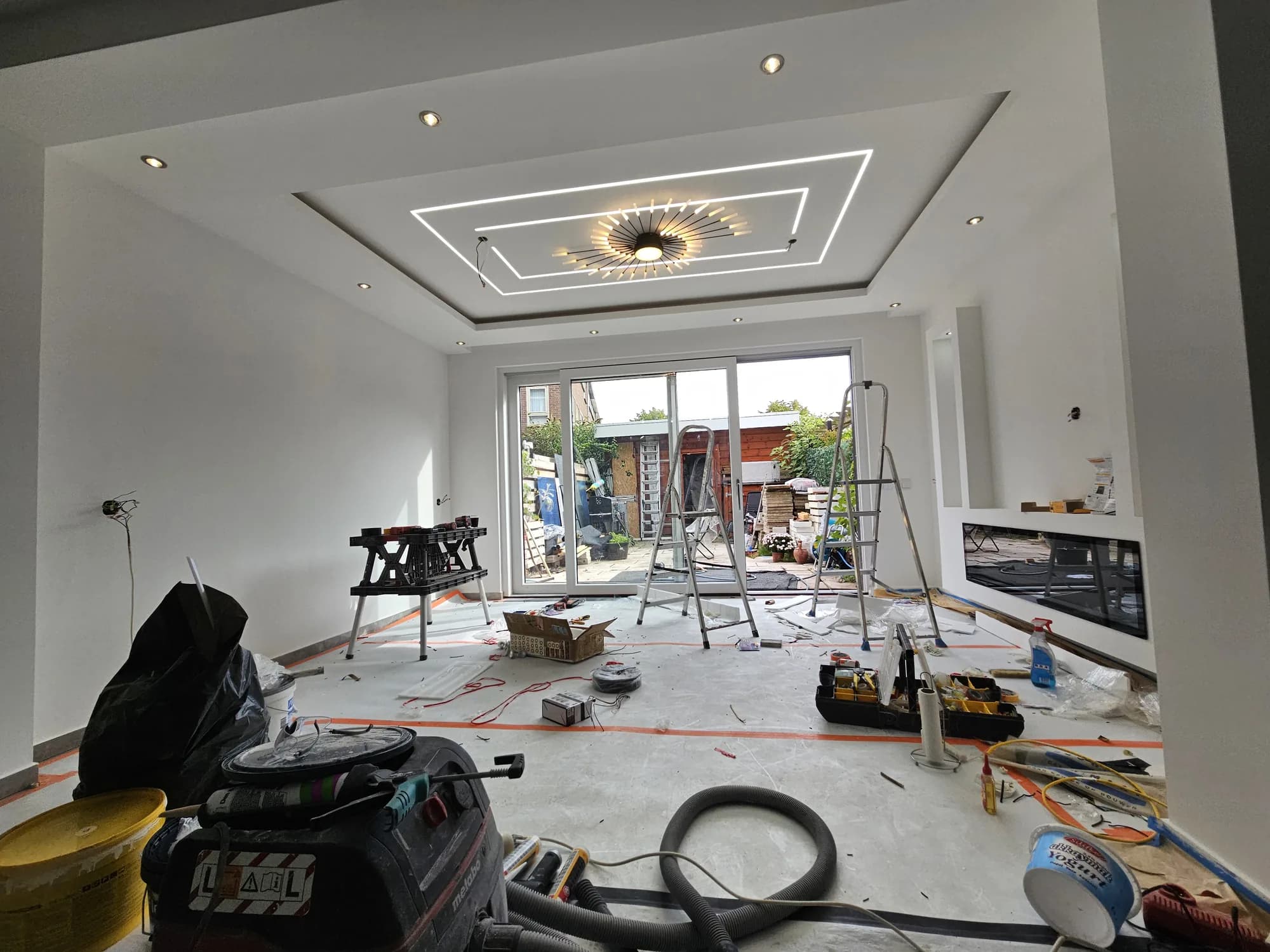 Woonkamer in de afbouwfase met gereedschap, zaagtafel en nieuw verlichtingsplafond