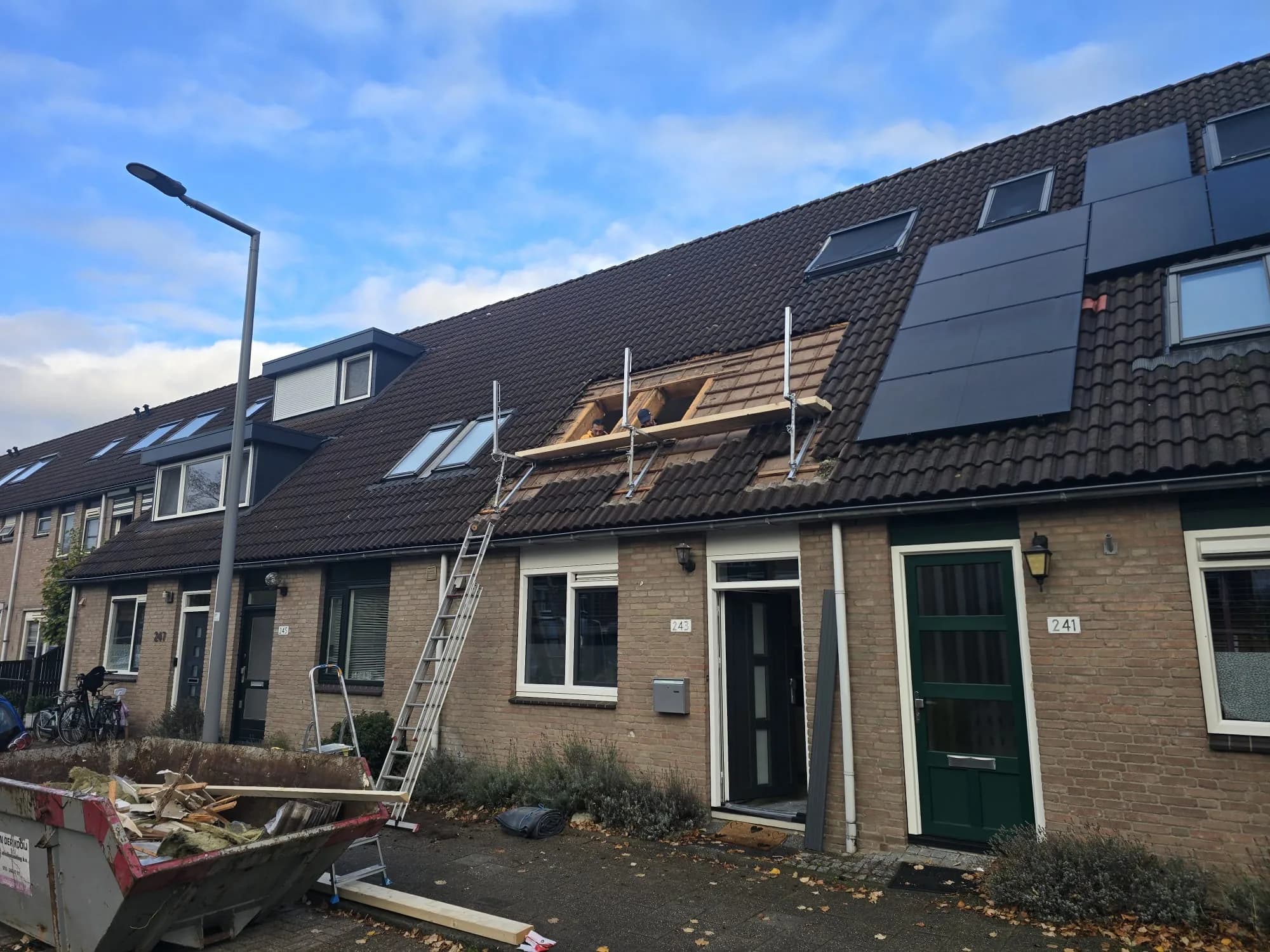 Rijtjeswoning met ladder en container tijdens dakwerkzaamheden, gezien vanaf de straat