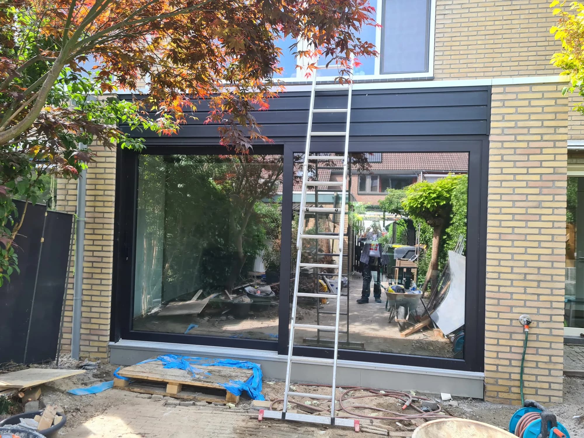 Moderne aanbouw met groot zwart kozijn aan de achterzijde van een rijtjeshuis tijdens de bouwfase