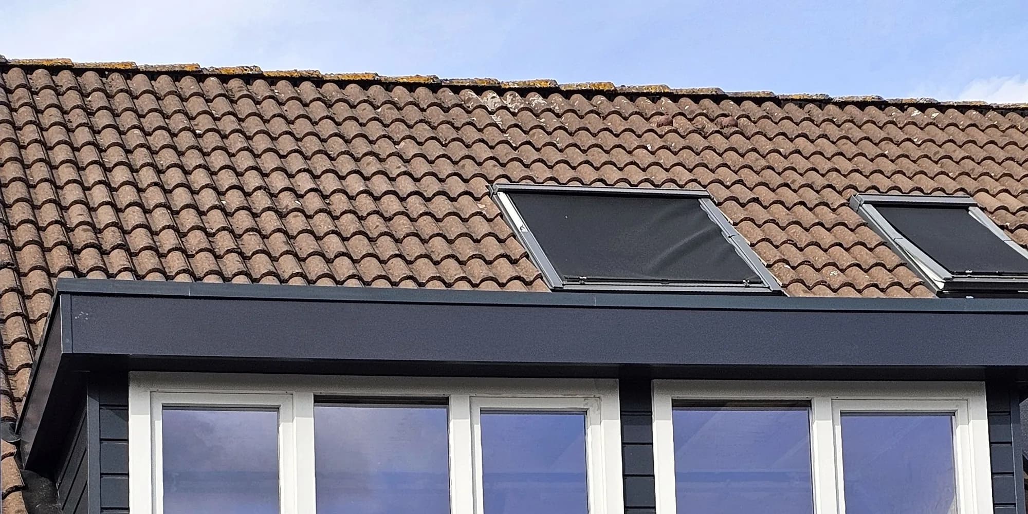 Afgewerkte antracietgrijze dakkapel met brede raampartij in een pannendak