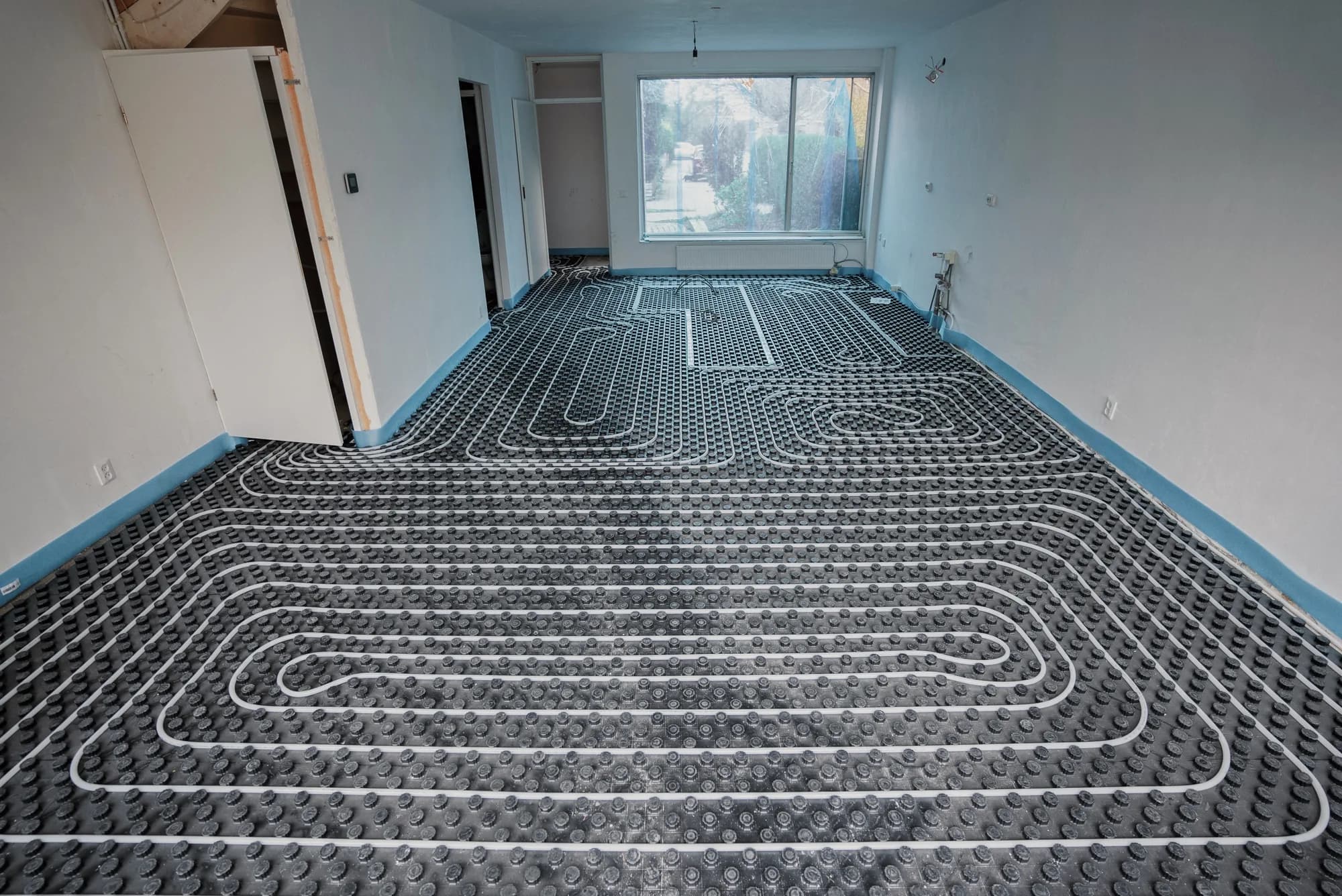 Vloerverwarmingsleidingen op noppenplaten in een woonkamer voor het storten van de afwerkvloer